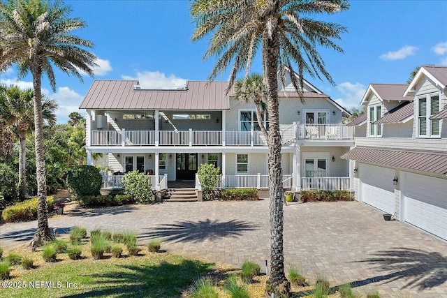 view of front facade featuring a balcony, an attached garage, covered porch, french doors, and decorative driveway