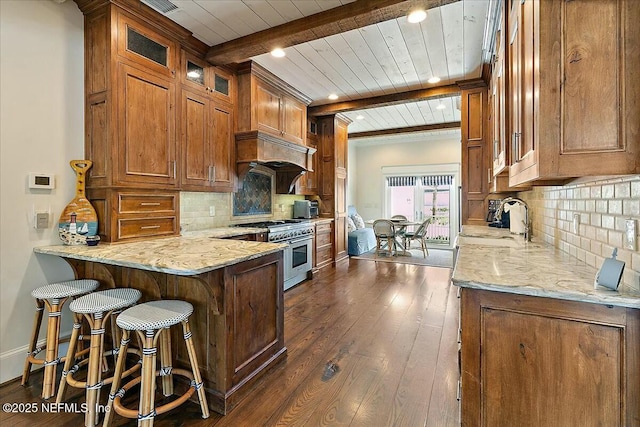 kitchen with light stone counters, brown cabinetry, a peninsula, range with two ovens, and dark wood-type flooring