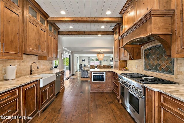 kitchen with a sink, open floor plan, stainless steel appliances, brown cabinetry, and custom exhaust hood