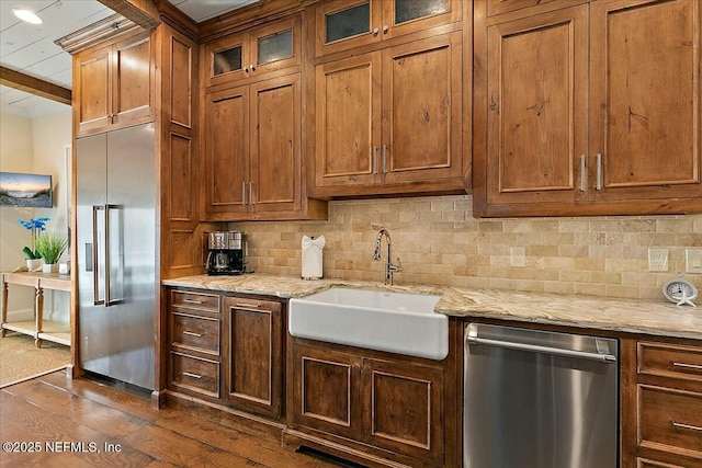 kitchen featuring tasteful backsplash, dark wood finished floors, brown cabinets, appliances with stainless steel finishes, and a sink