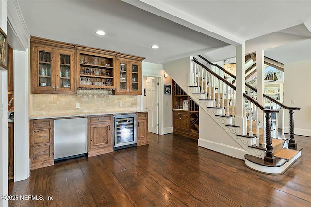 bar featuring dark wood-type flooring, wine cooler, stairway, a bar, and fridge