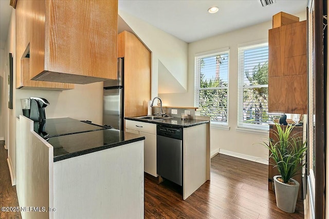 kitchen with dark wood-type flooring, a sink, dark countertops, appliances with stainless steel finishes, and a peninsula