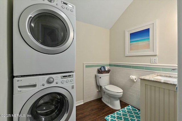 washroom with stacked washer / dryer, a sink, laundry area, wainscoting, and dark wood-style flooring