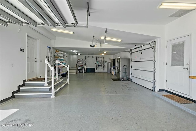 garage featuring a garage door opener, visible vents, freestanding refrigerator, and baseboards