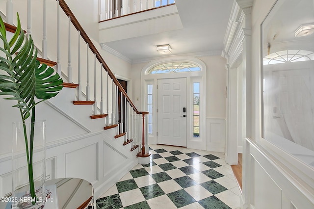 entrance foyer featuring ornamental molding, stairway, wainscoting, a decorative wall, and light floors