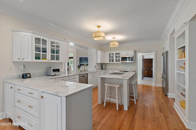 kitchen featuring a peninsula, light wood-style flooring, stainless steel appliances, glass insert cabinets, and white cabinetry