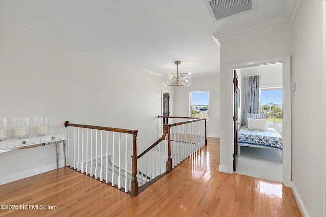 hallway with visible vents, light wood-style floors, crown molding, a notable chandelier, and an upstairs landing