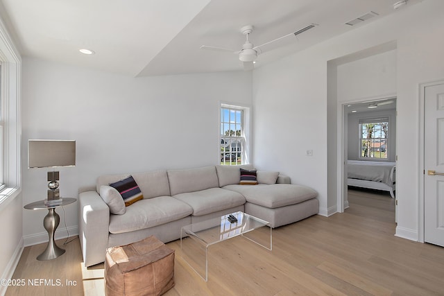 living room with visible vents, light wood-style flooring, baseboards, lofted ceiling, and ceiling fan