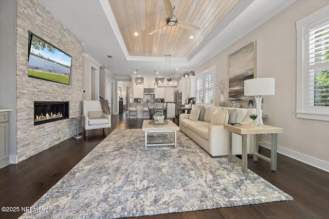 living area featuring baseboards, dark wood finished floors, a stone fireplace, wood ceiling, and a raised ceiling