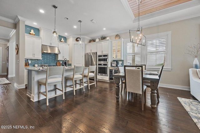 kitchen featuring backsplash, dark wood-style flooring, under cabinet range hood, and ornamental molding