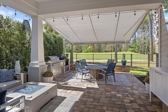 view of patio featuring outdoor dining space, fence, grilling area, a fire pit, and exterior kitchen