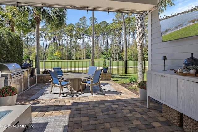 view of patio with outdoor dining space, an outdoor kitchen, fence, and a grill