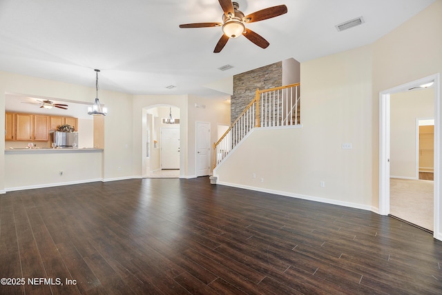 unfurnished living room with dark wood-style floors, ceiling fan with notable chandelier, and arched walkways