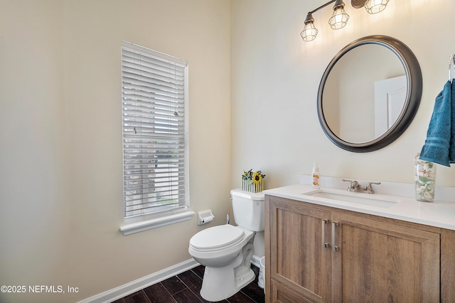 half bathroom with vanity, toilet, wood finished floors, and baseboards