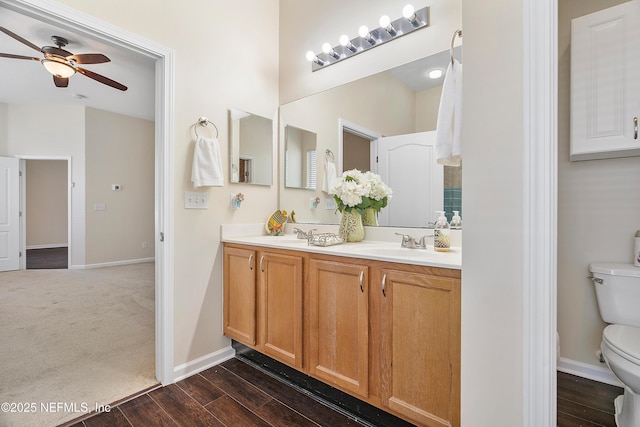 full bath with wood finished floors, a ceiling fan, baseboards, double vanity, and toilet