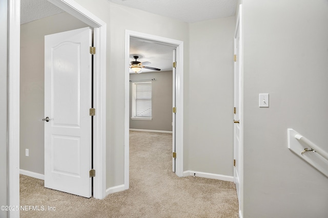 corridor featuring light colored carpet, a textured ceiling, and baseboards