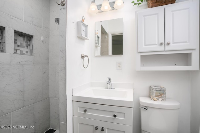 bathroom featuring toilet, vanity, and a tile shower