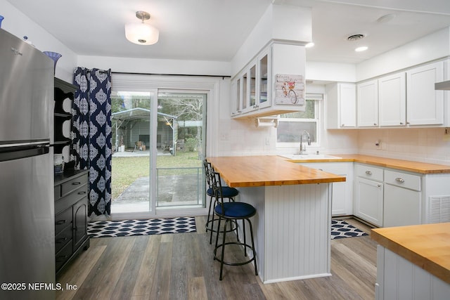 kitchen featuring a breakfast bar, a sink, freestanding refrigerator, glass insert cabinets, and wooden counters