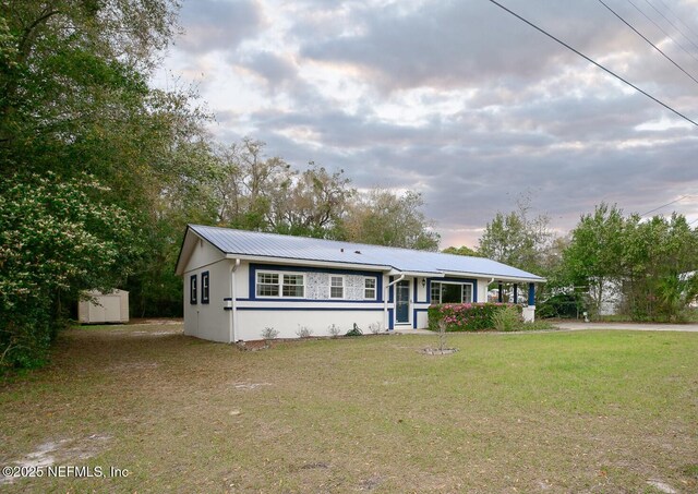 ranch-style home featuring stucco siding, an outbuilding, a front lawn, a storage shed, and metal roof