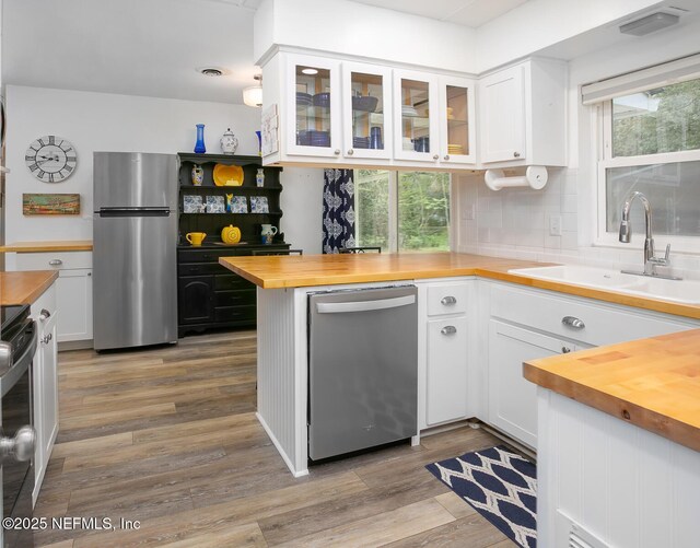 kitchen featuring wooden counters, a sink, stainless steel appliances, light wood-style floors, and white cabinetry