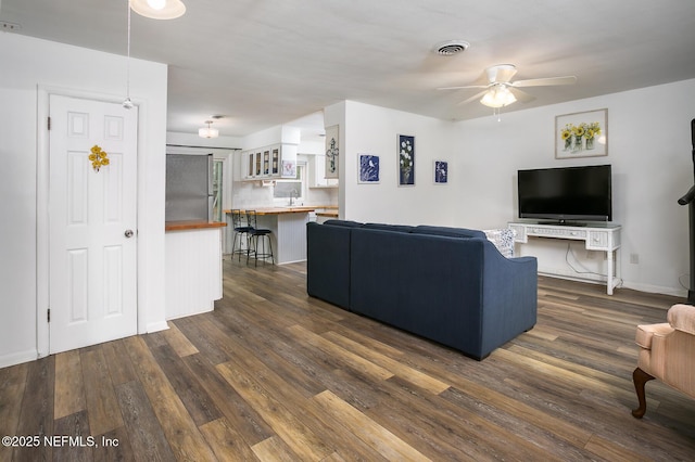 living room with dark wood finished floors, a ceiling fan, visible vents, and baseboards