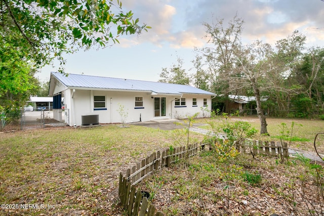 rear view of property with stucco siding, a lawn, a patio, fence, and metal roof