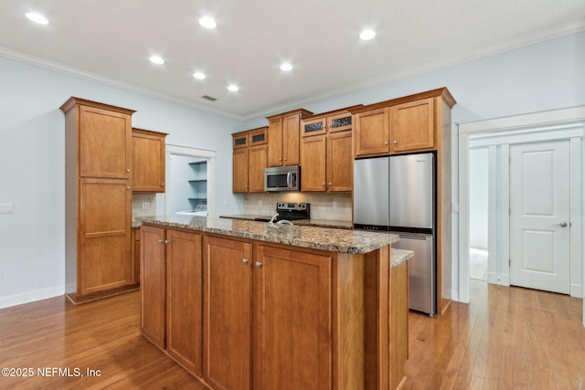 kitchen with brown cabinets, appliances with stainless steel finishes, stone countertops, and light wood-type flooring