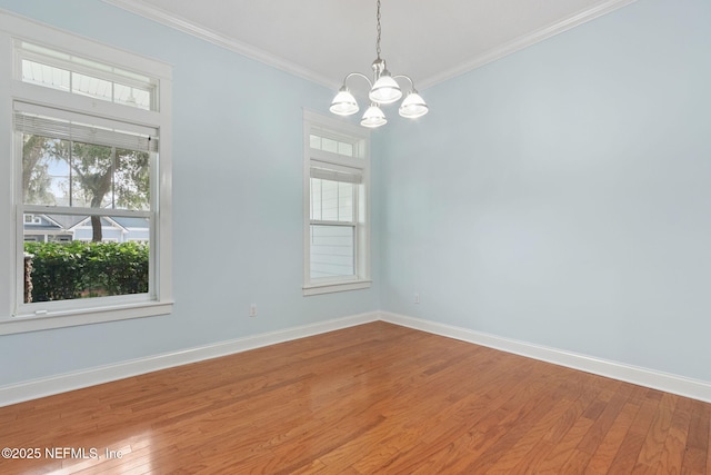 spare room with a chandelier, baseboards, hardwood / wood-style floors, and crown molding