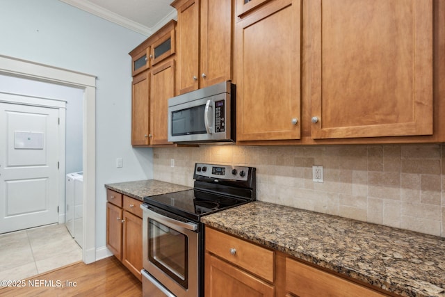 kitchen featuring brown cabinetry, washer / dryer, dark stone counters, appliances with stainless steel finishes, and crown molding