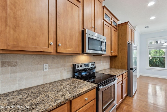 kitchen with stainless steel appliances, brown cabinets, light wood-style floors, and dark stone counters