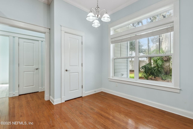 unfurnished dining area featuring a chandelier, crown molding, baseboards, and wood-type flooring