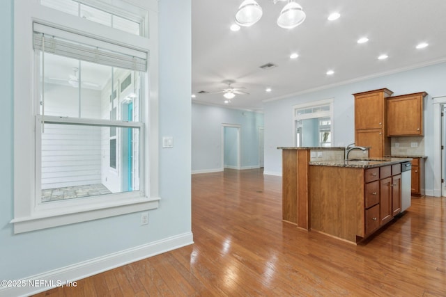 kitchen with visible vents, a ceiling fan, a sink, dark stone counters, and brown cabinetry