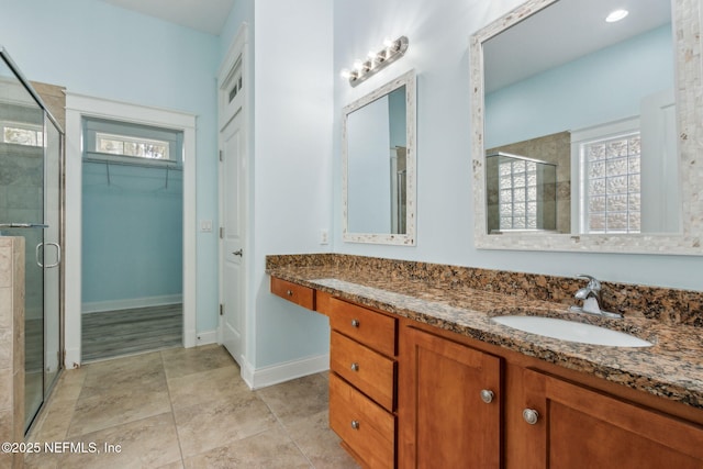 bathroom featuring a walk in closet, a shower stall, tile patterned flooring, baseboards, and vanity