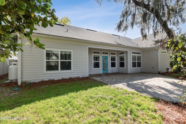 rear view of house featuring a patio, a yard, and a shingled roof