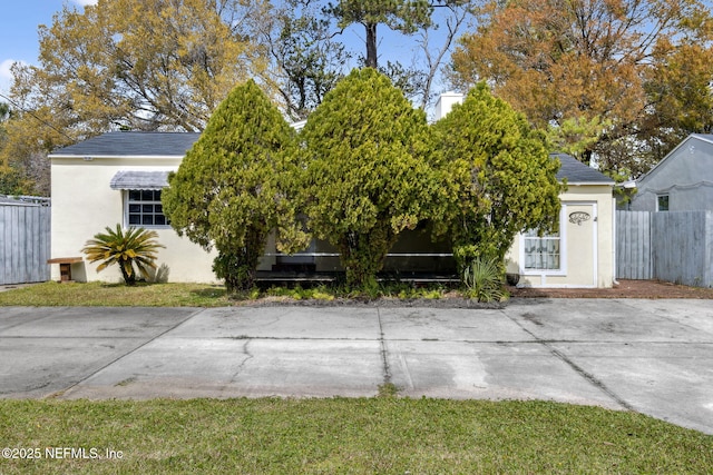 view of property hidden behind natural elements with fence, roof with shingles, and stucco siding