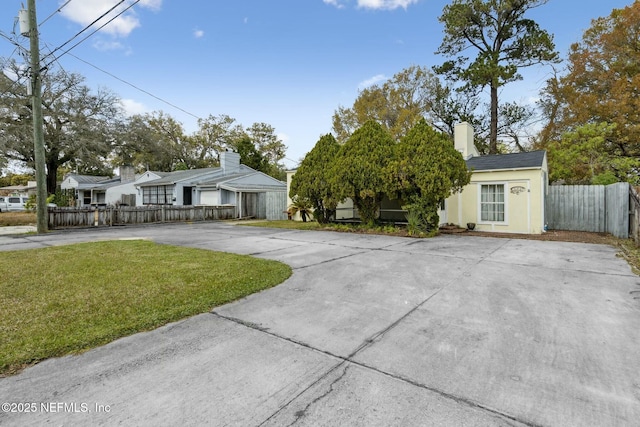 view of front of house featuring stucco siding, driveway, fence, a front yard, and a chimney