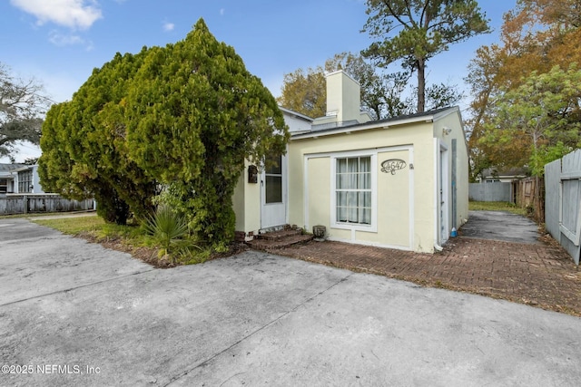 view of front of home featuring stucco siding, entry steps, a chimney, and fence