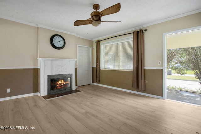 unfurnished living room featuring ornamental molding, a glass covered fireplace, wood finished floors, baseboards, and ceiling fan