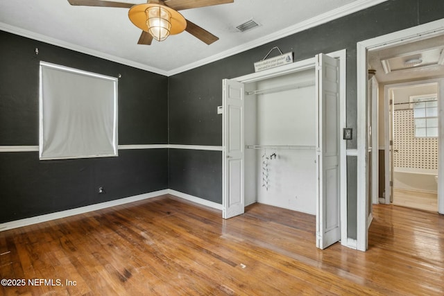 unfurnished bedroom with visible vents, crown molding, baseboards, hardwood / wood-style flooring, and a closet