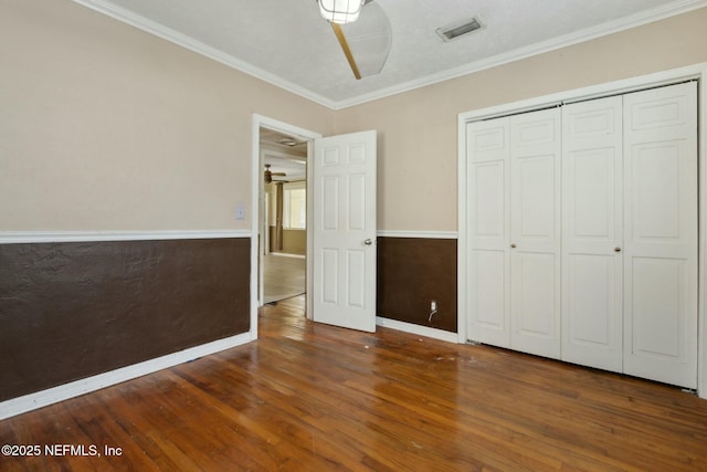 unfurnished bedroom featuring visible vents, wood finished floors, a closet, crown molding, and baseboards