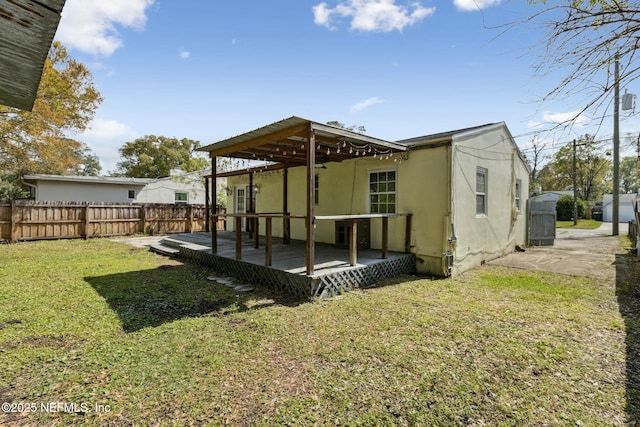 back of house featuring a wooden deck, fence, a lawn, and stucco siding