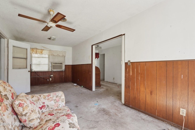 unfurnished room with wooden walls, ceiling fan, a wainscoted wall, cooling unit, and a textured ceiling