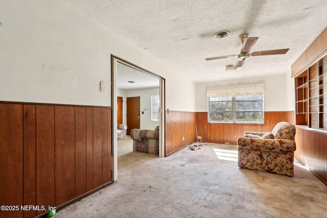 living area with a ceiling fan, carpet, a wainscoted wall, wood walls, and a textured ceiling