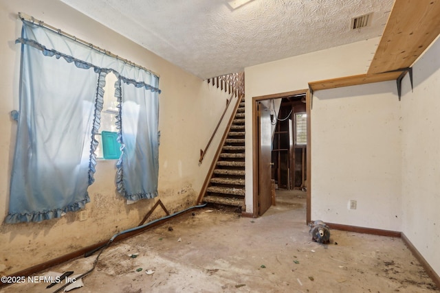 below grade area featuring visible vents, a textured ceiling, stairs, and baseboards