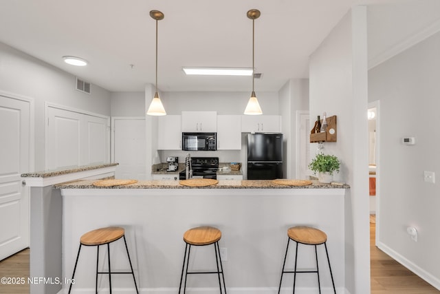 kitchen with visible vents, black appliances, a breakfast bar, white cabinetry, and light wood-style floors