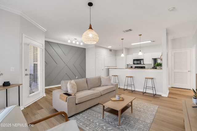 living room featuring visible vents, ornamental molding, an accent wall, and light wood finished floors