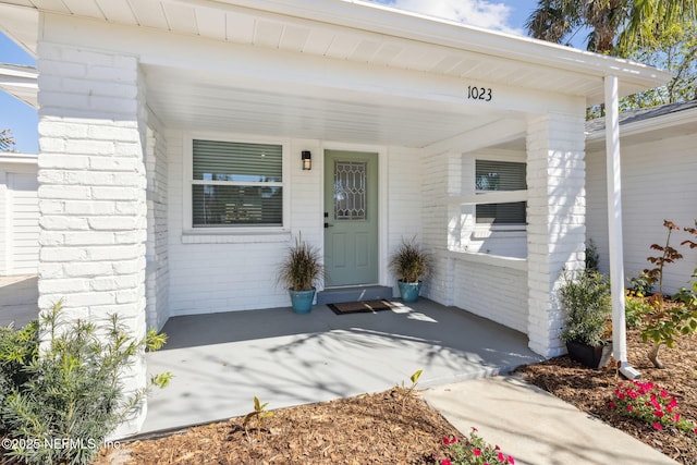 entrance to property featuring covered porch and brick siding