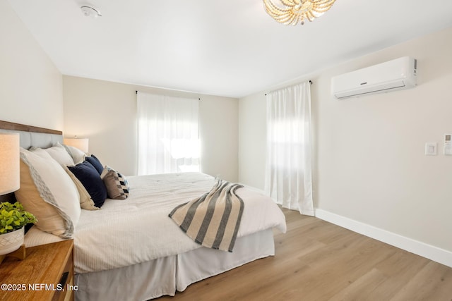 bedroom with wood finished floors, baseboards, and a wall mounted AC