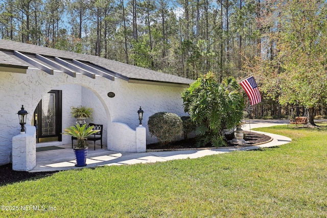 view of side of home featuring a lawn, roof with shingles, and stucco siding