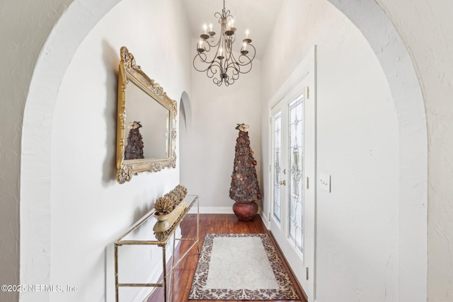 entryway featuring arched walkways, a chandelier, baseboards, and wood finished floors